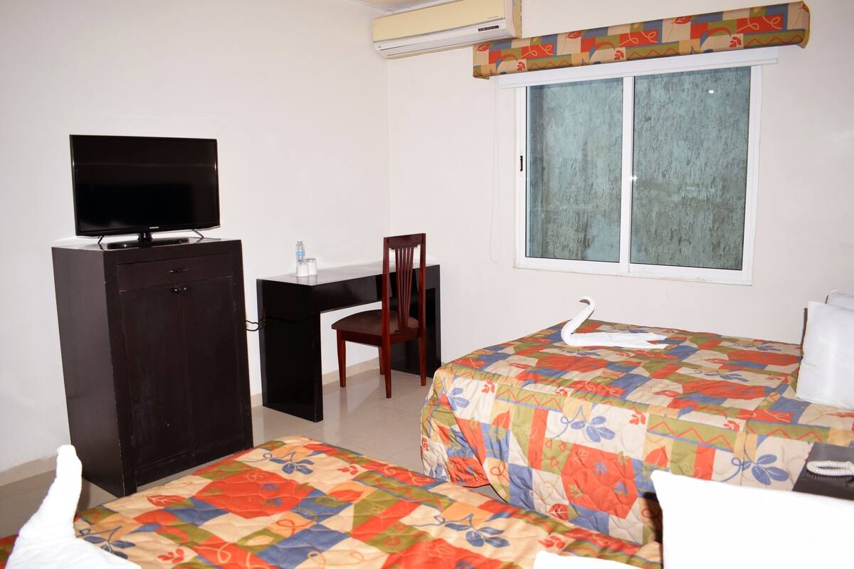Quarto com cama, escrivaninha, cadeira e televisão.