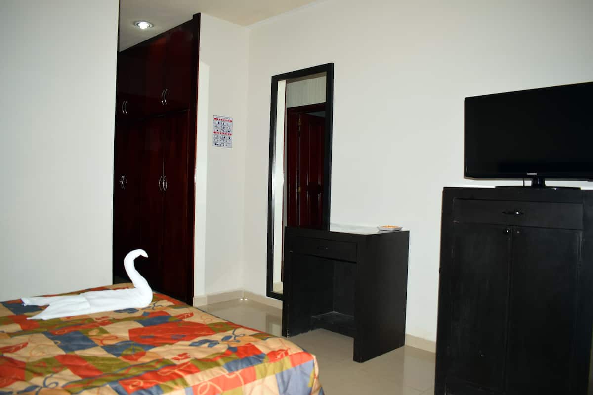 Quarto de hotel com uma cama, penteadeira, televisão e espelho.