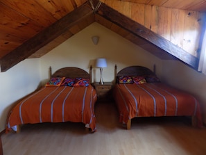 Un dormitorio acogedor y pequeño en el ático, con dos camas individuales, vigas de madera, una mesita de noche con lámpara y techo inclinado.
