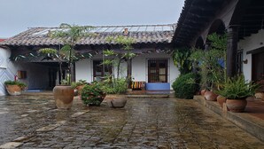 A courtyard with a tiled floor, potted plants, and a building with a tiled roof and white walls. - Kukurutz Residencia (San Cristóbal de las Casas)