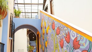 A narrow corridor with a colorful mural, a glass ceiling, and potted plants. - Kukurutz Residencia (San Cristóbal de las Casas)
