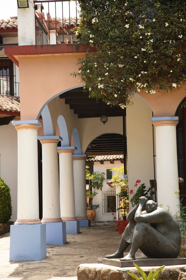 Un patio con una estatua, columnas y un edificio de techo a tejas.