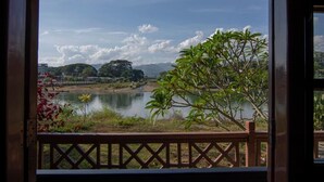 A view from a window with a wooden railing, overlooking a calm lake, surrounded by greenery and distant hills. - Riverside @ Hsipaw Resort (Hsipaw)