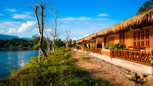 A thatched-roof building with a wooden fence and a pathway leading to a body of water. - Riverside @ Hsipaw Resort (Hsipaw)