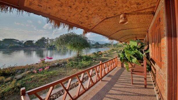 A covered veranda with a view of a lake and greenery. - Riverside @ Hsipaw Resort (Hsipaw)