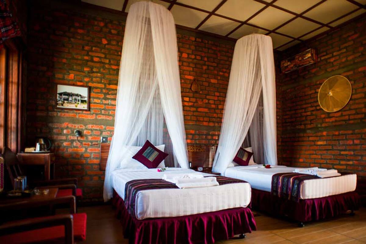 Una habitación con dos camas, cada una con ropa blanca y colchas rojas, y una pared de ladrillo.