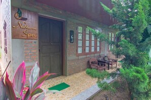 A brick building with a wooden door and windows, a sign reading "Nibbana Spa", and outdoor furniture.