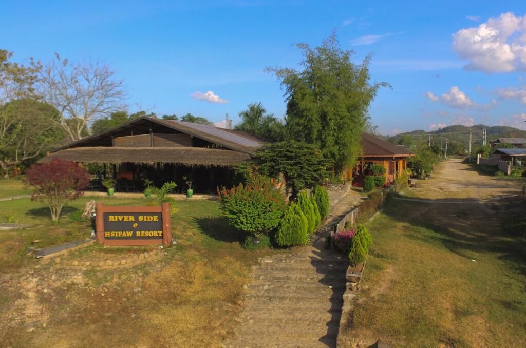 A rustic building with a thatched roof, surrounded by greenery and a sign reading "River Side Hsipay Resort".