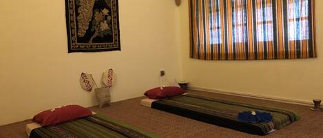 Ein Zimmer mit zwei Meditationsmatten, einer Wandtextil, einer Topfpflanze und einem gestreiften Vorhang.