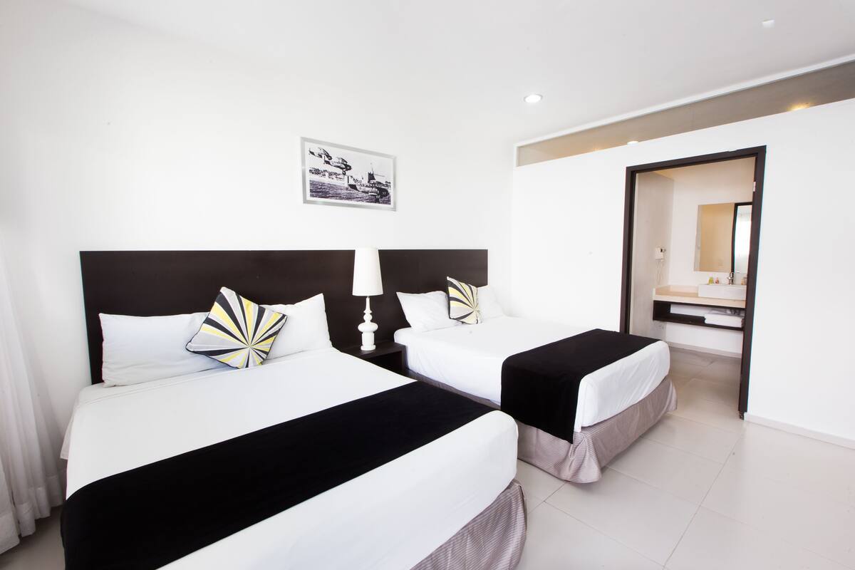A hotel room with two beds, a nightstand with a lamp, a framed picture on the wall, and a mirror in the corner.