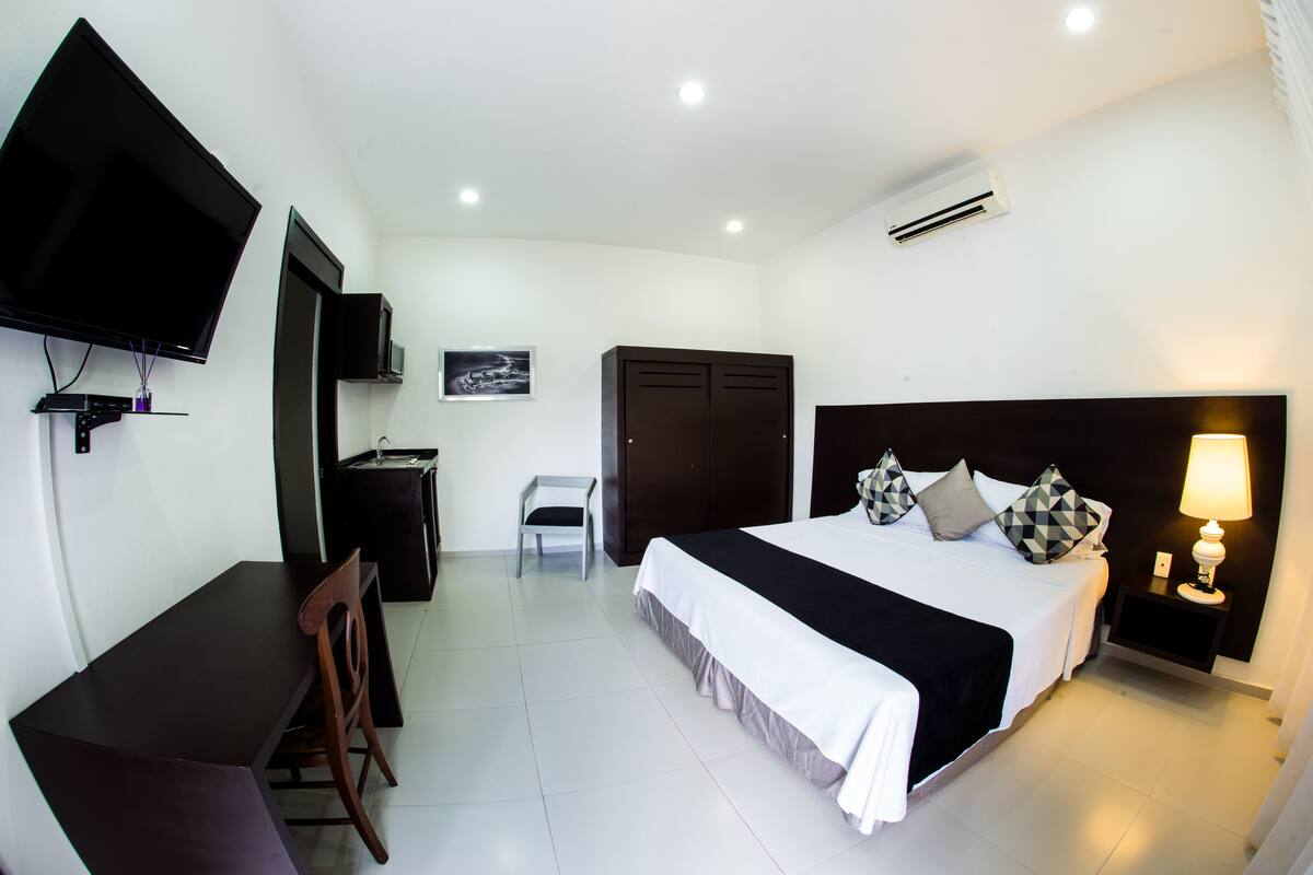 A hotel room with a bed, desk, chair, TV, wardrobe, and bedside lamp.