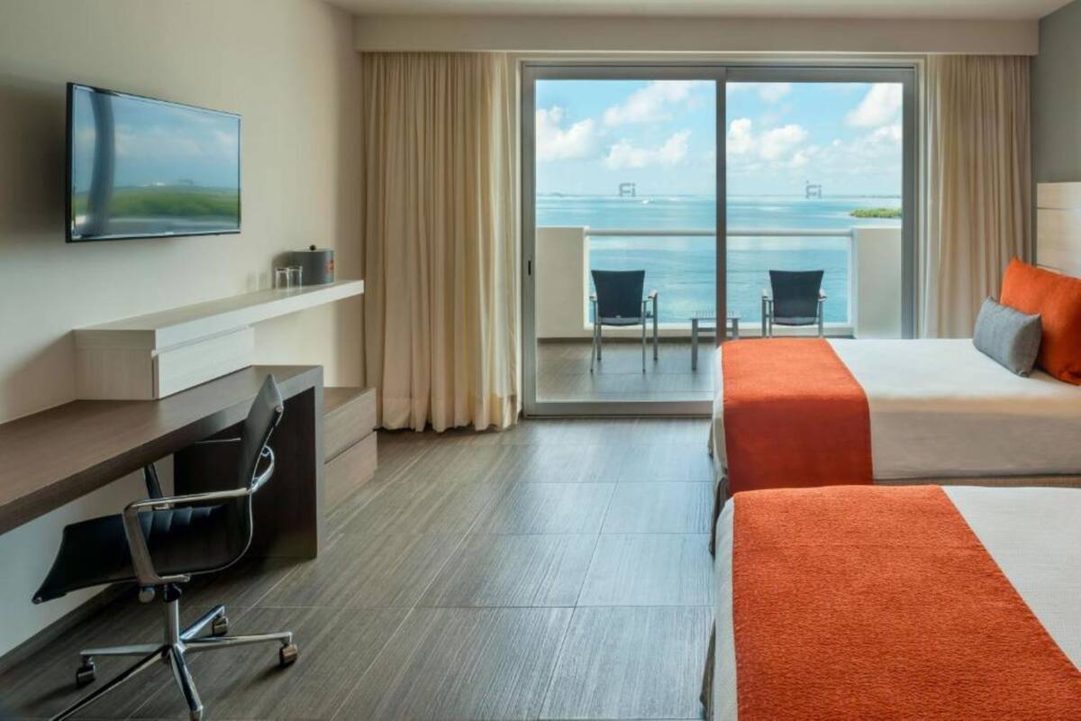A hotel room with a balcony, a desk, two beds, and a TV.