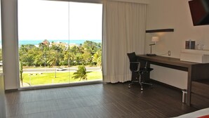 A hotel room with a large sliding glass door to the ocean, a desk with a chair, a TV mounted on the wall, and a lamp. - Real Inn Cancun (Cancun)