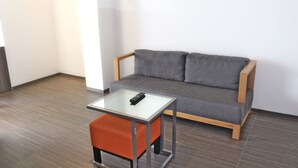 A modern room with a grey sofa, a small orange ottoman, and a glass-top table with a remote control. - Real Inn Cancun (Cancun)