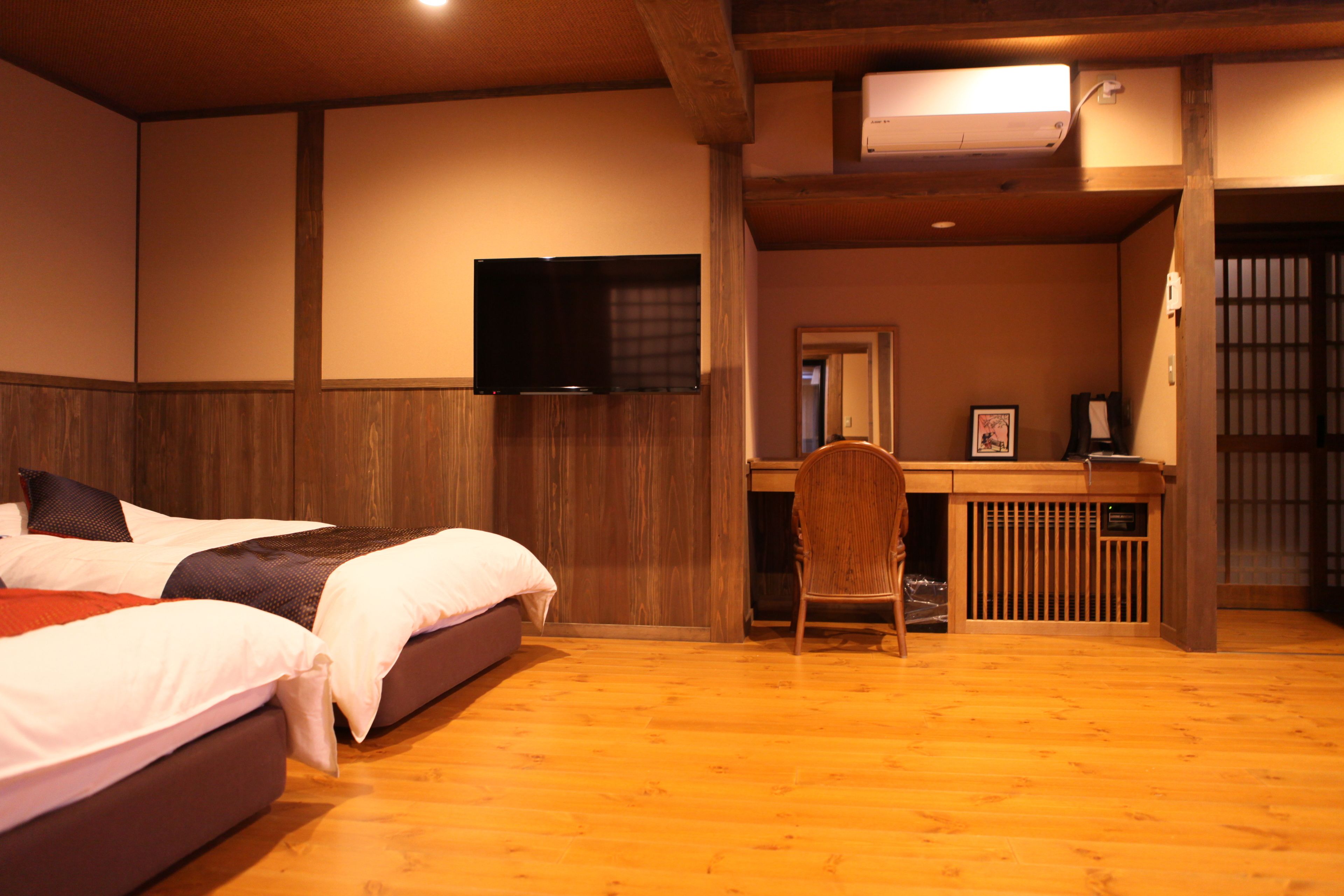 Una habitación de hotel con cama, escritorio, silla, televisor y piso de madera.