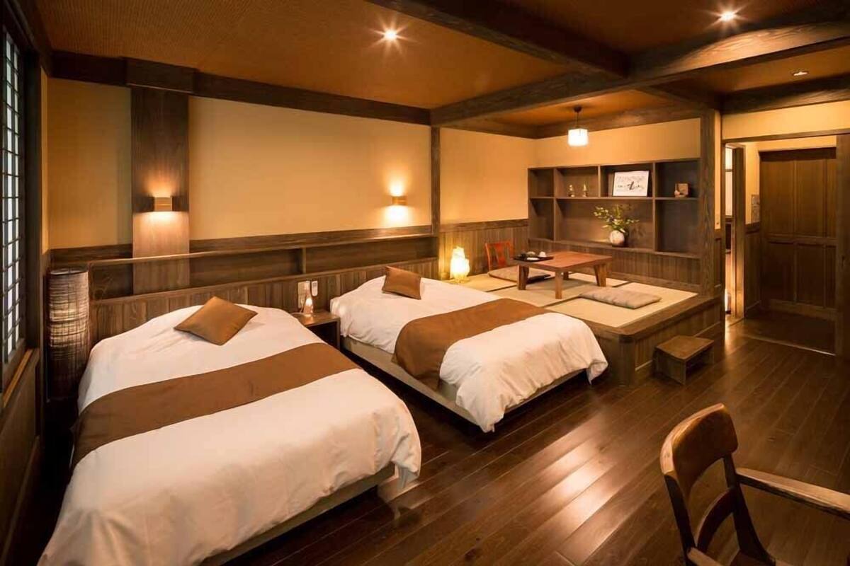A room with two beds, a wooden floor, a table, and a chair.