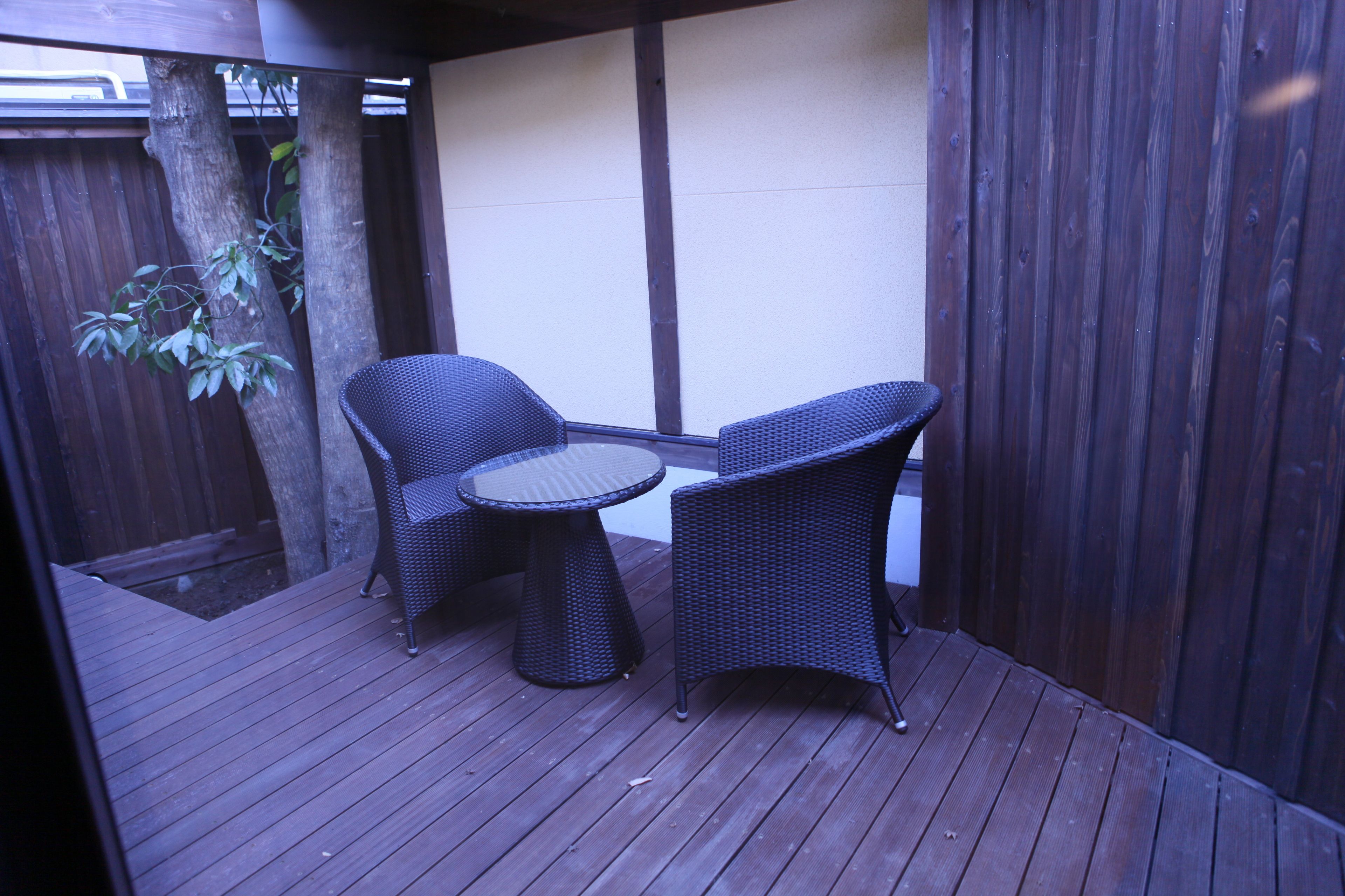 A wooden deck with two wicker chairs and a small round table.