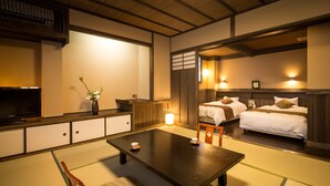 A traditional Japanese-style room with tatami flooring, a low table, a TV, and two beds with pillows and a nightstand. - Kurokawa Onsen Ryokan Wakaba (Minamioguni)