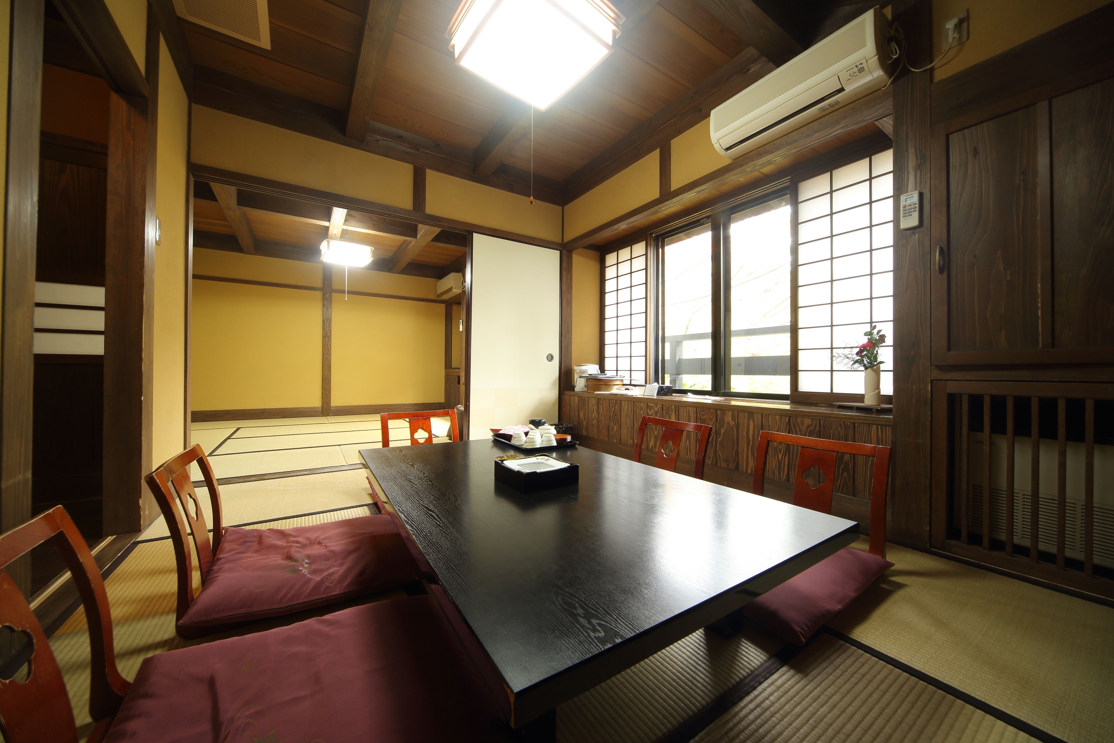 A traditional Japanese room with tatami flooring, a low table, wooden chairs, and sliding doors.
