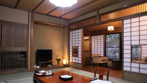 A traditional Japanese room with tatami flooring, a low table with cushions, a television, and sliding doors leading to another room. - Kurokawa Onsen Ryokan Wakaba (Minamioguni)