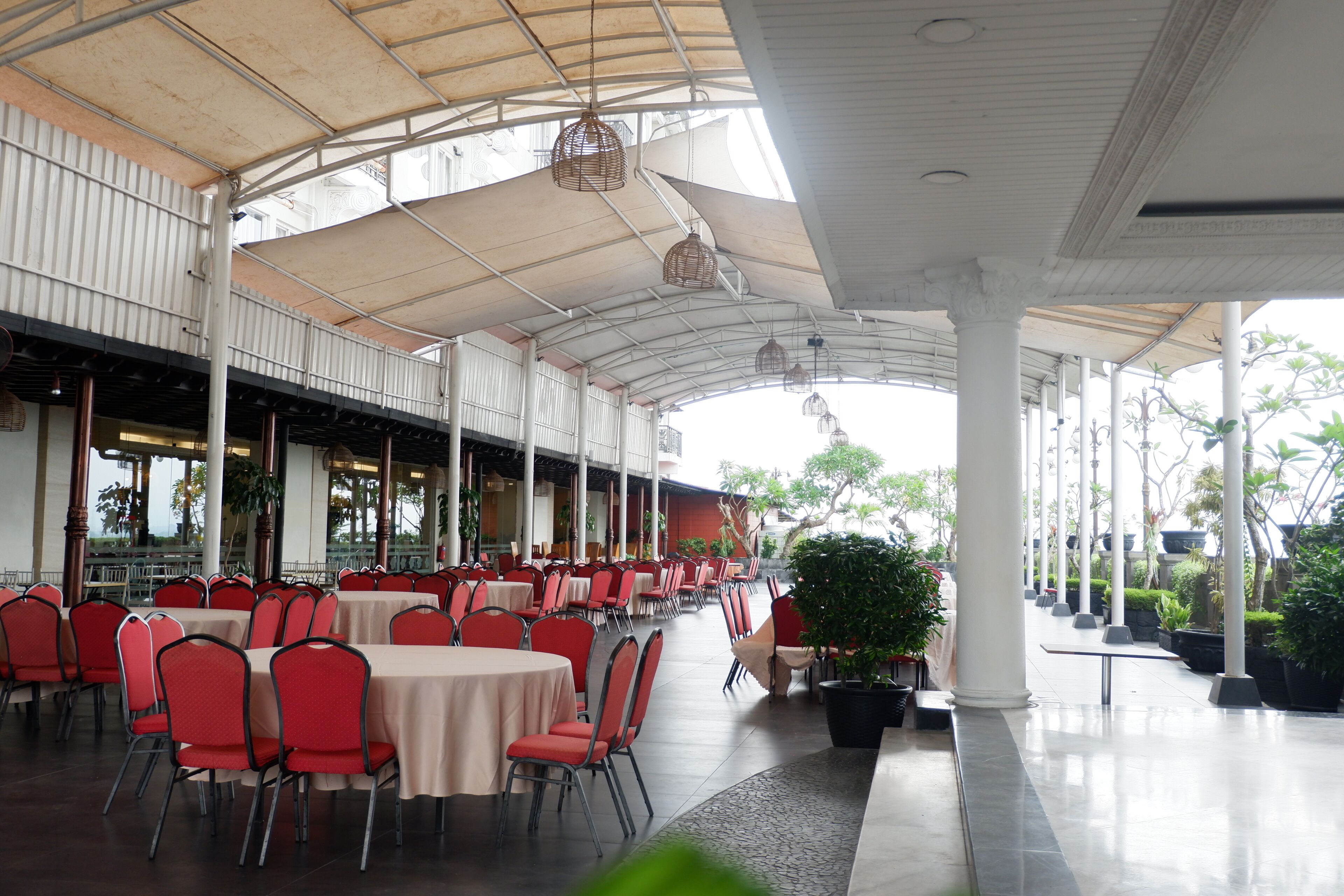 A covered outdoor dining area with tables and chairs, columns, and potted plants.