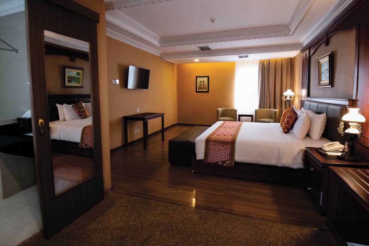 Habitación de hotel con una cama grande, un escritorio, una silla, un televisor y un espejo.