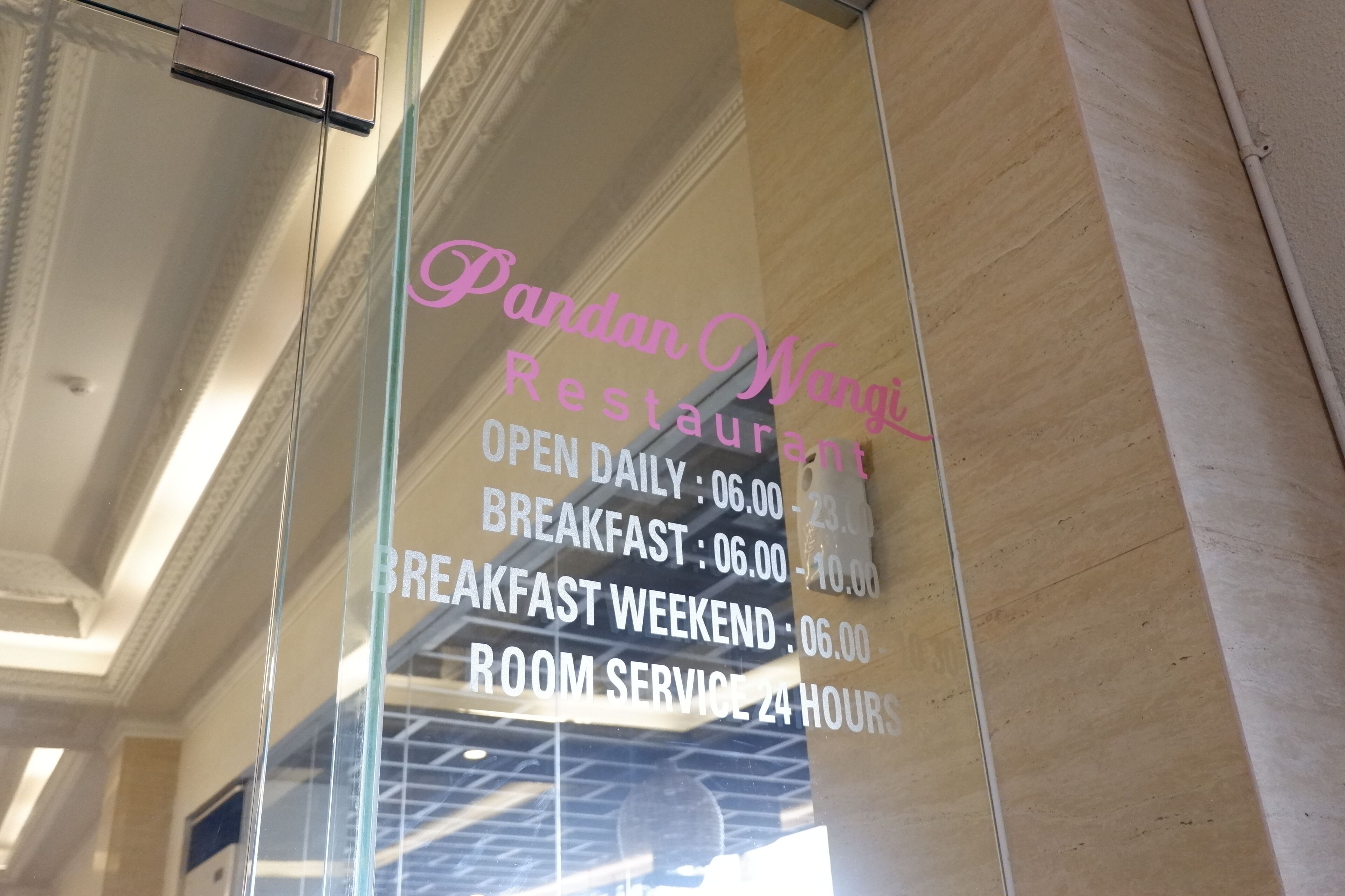 A glass window with text advertising a restaurant's opening hours and room service availability.