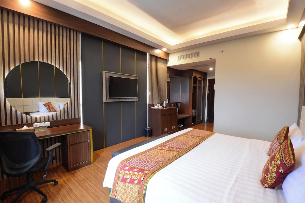 Una habitación de hotel con cama, escritorio, silla, televisor y armario.