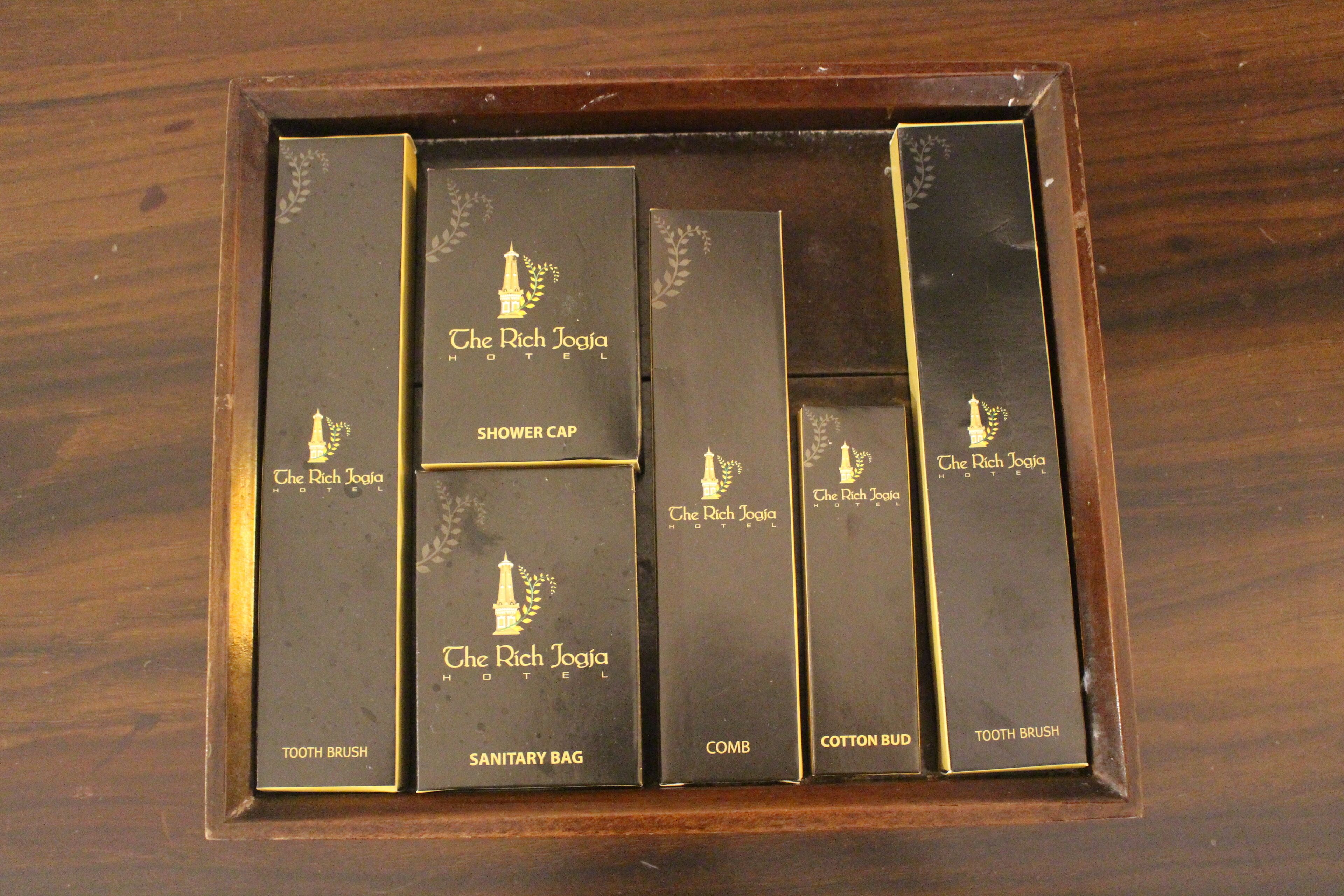 A set of toiletries in a wooden box with labels for a toothbrush, comb, sanitary bag, shower cap, and cotton bud.