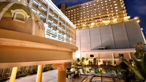 Un hotel de varios pisos, con un amplio área de piscina y una fuente.