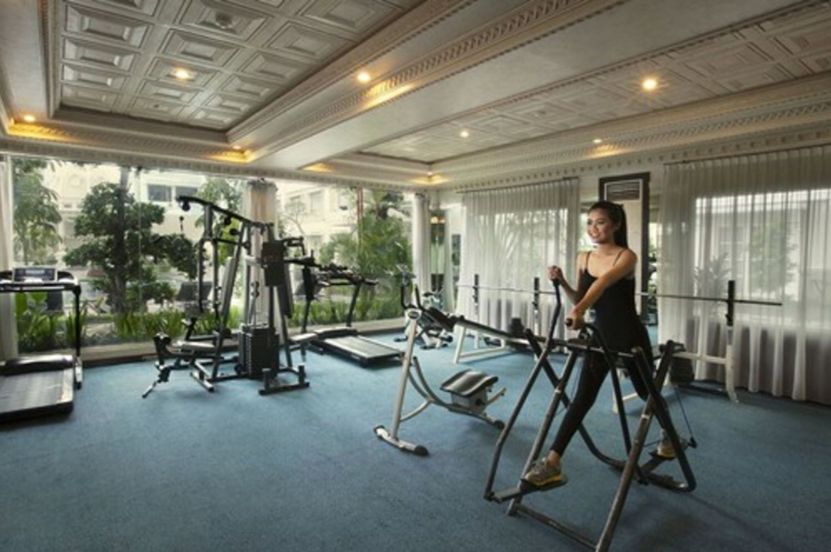 A gym with exercise equipment, large windows, and a view of greenery outside.