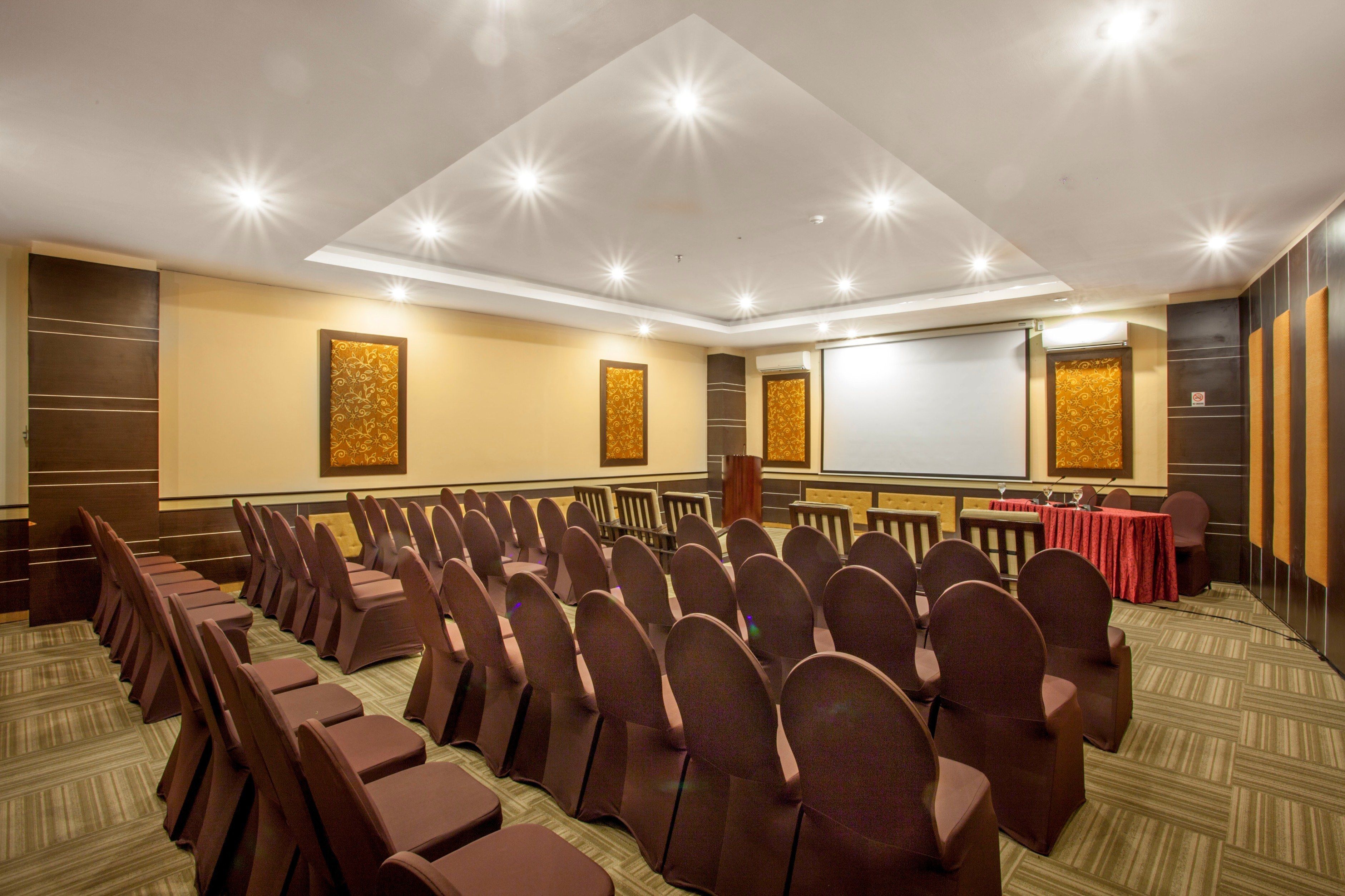A conference room with rows of chairs, a projector screen, and a podium.