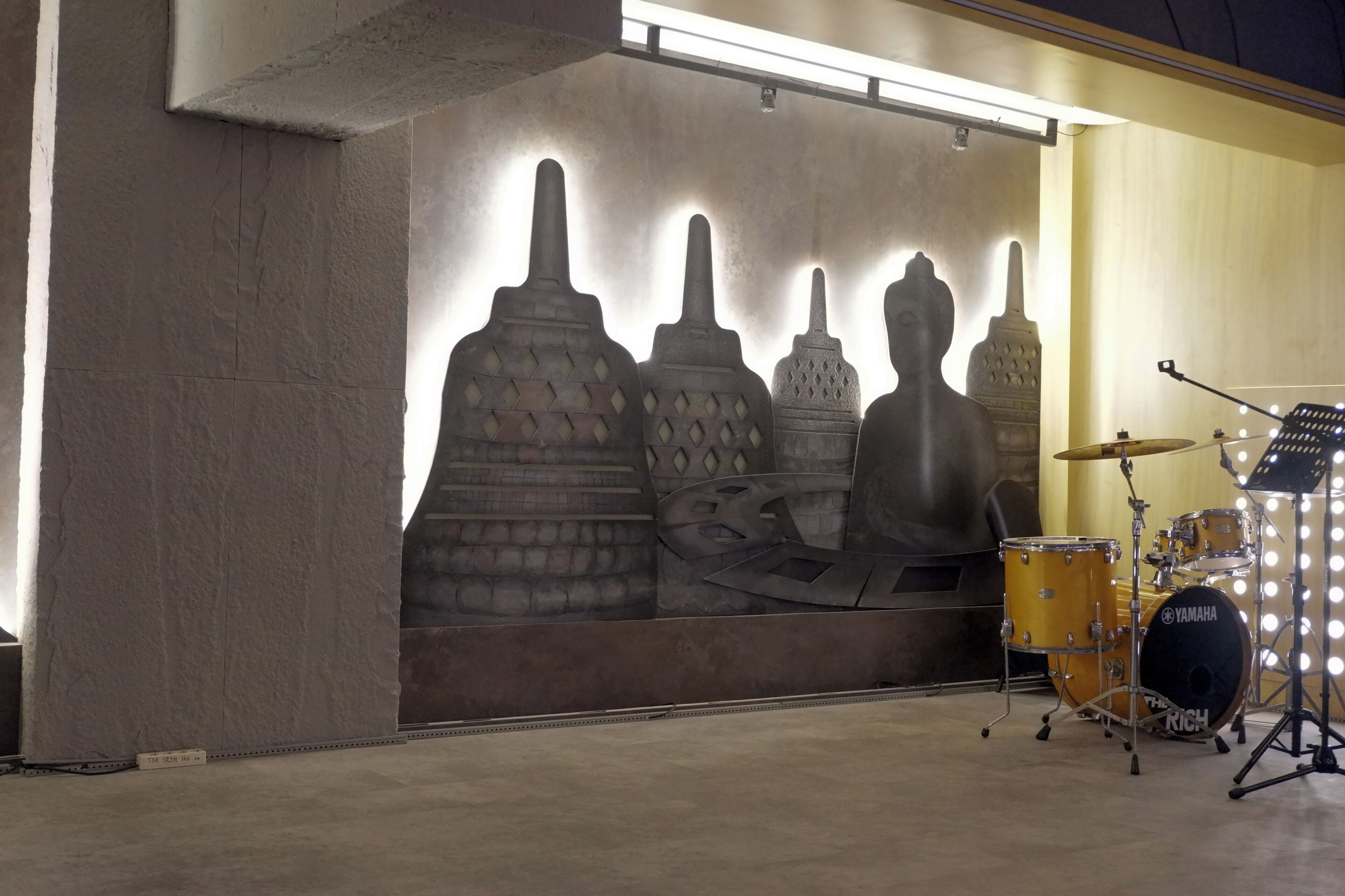 A drum set with a Yamaha logo, a wall with abstract sculptures, and a light fixture.