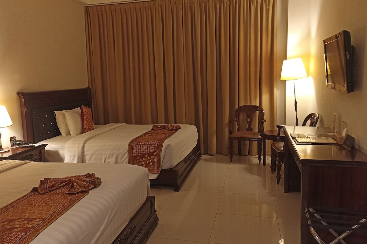 Una habitación de hotel con dos camas, un escritorio, una silla y una lámpara.