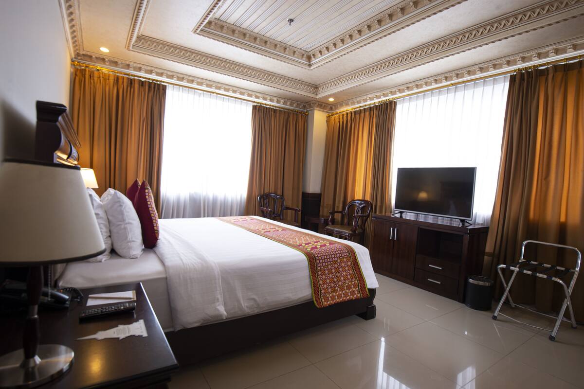 Habitación de hotel con una cama grande, un televisor, un escritorio con lámpara y una silla.