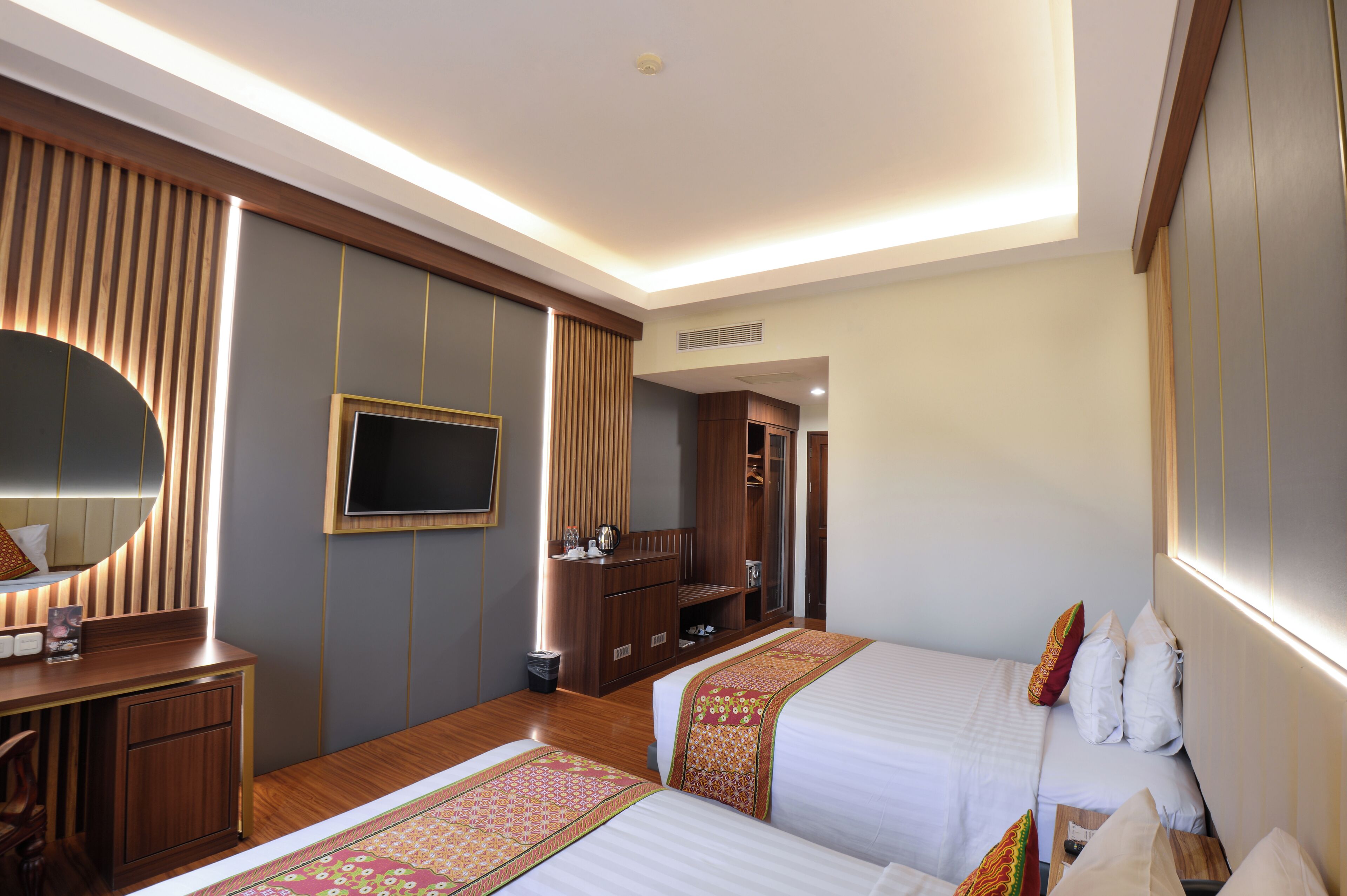 A hotel room with two beds, a TV, a wooden dresser, and a wardrobe.