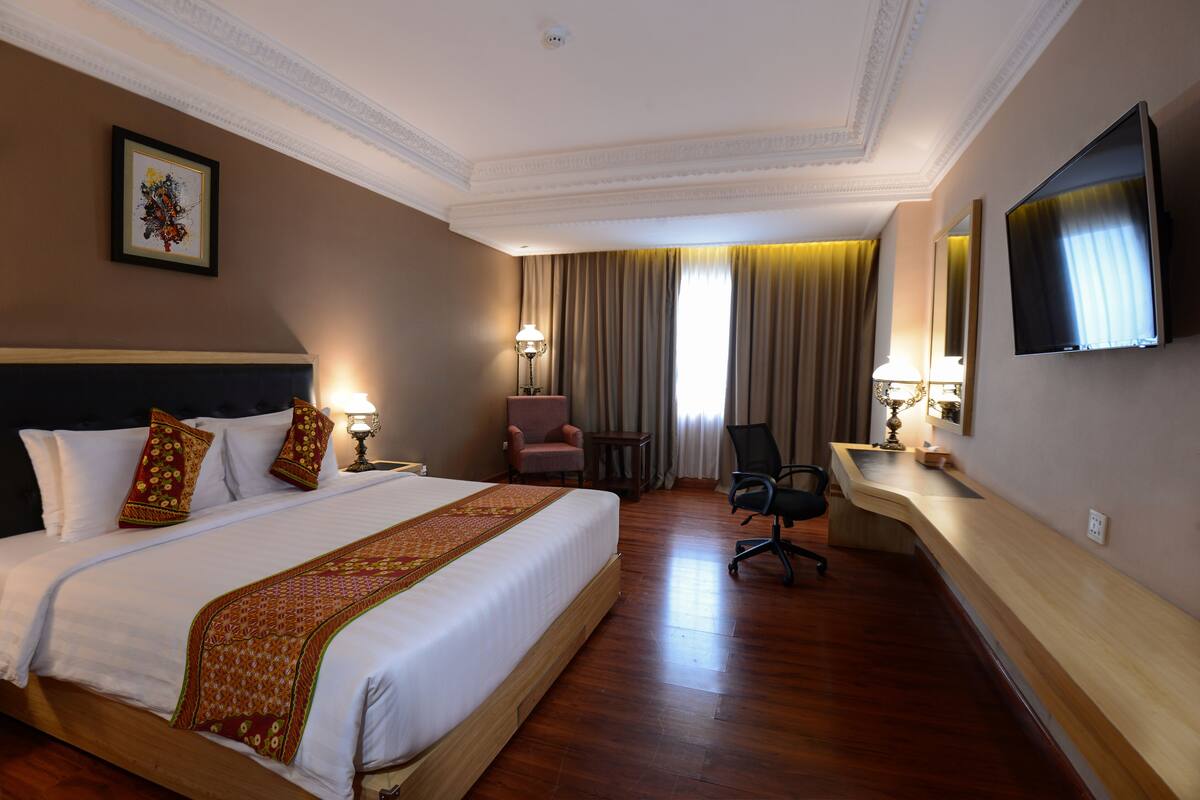 Habitación de hotel con una cama grande, un escritorio, una silla, un televisor y una ventana con cortinas.