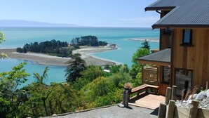 A wooden house with a balcony overlooking a coastal landscape with a clear view of the sea and a small island. - The Wheelhouse Inn (Nelson)