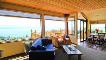 A spacious room with a large window overlooking the sea, a wooden ceiling, and a cozy seating area with a sofa and a table.