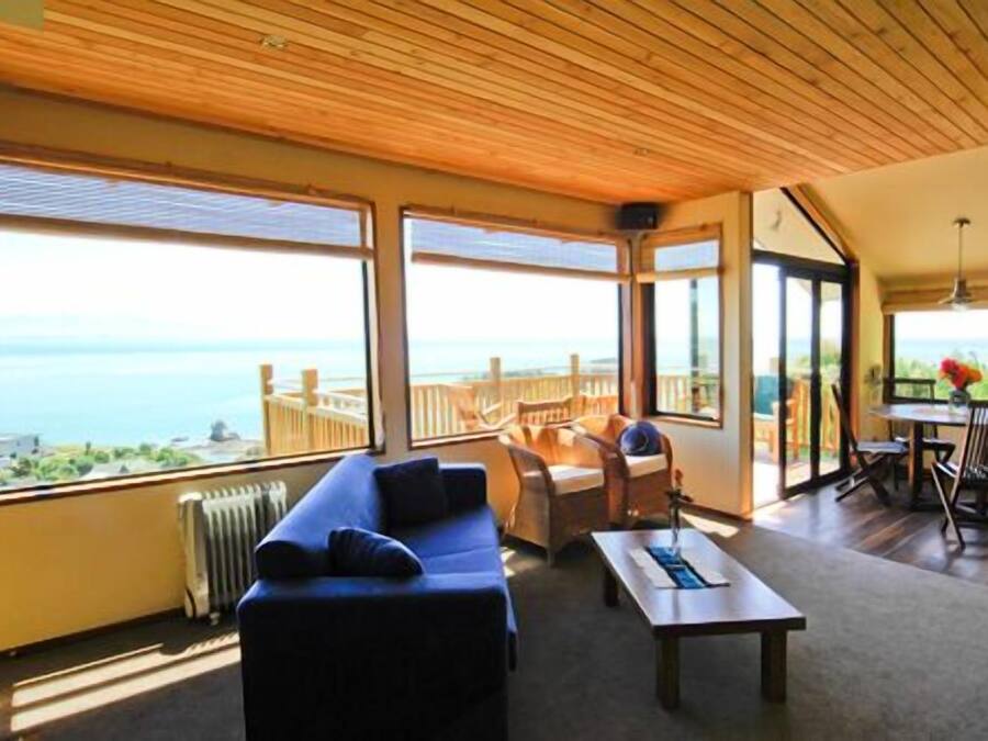 A spacious room with a large window overlooking the sea, a wooden ceiling, and a cozy seating area with a sofa and a table.