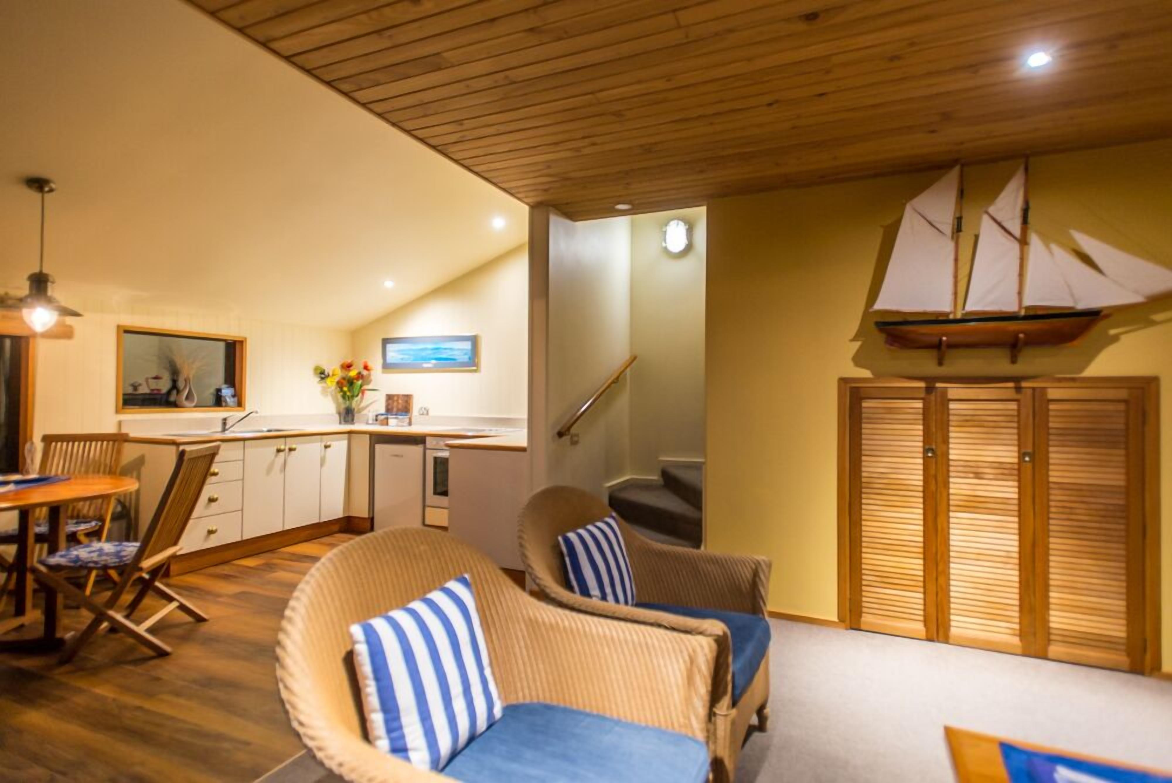 Een gezellige woonkamer met rieten meubels, een trap en een decoratie van een zeilboot.