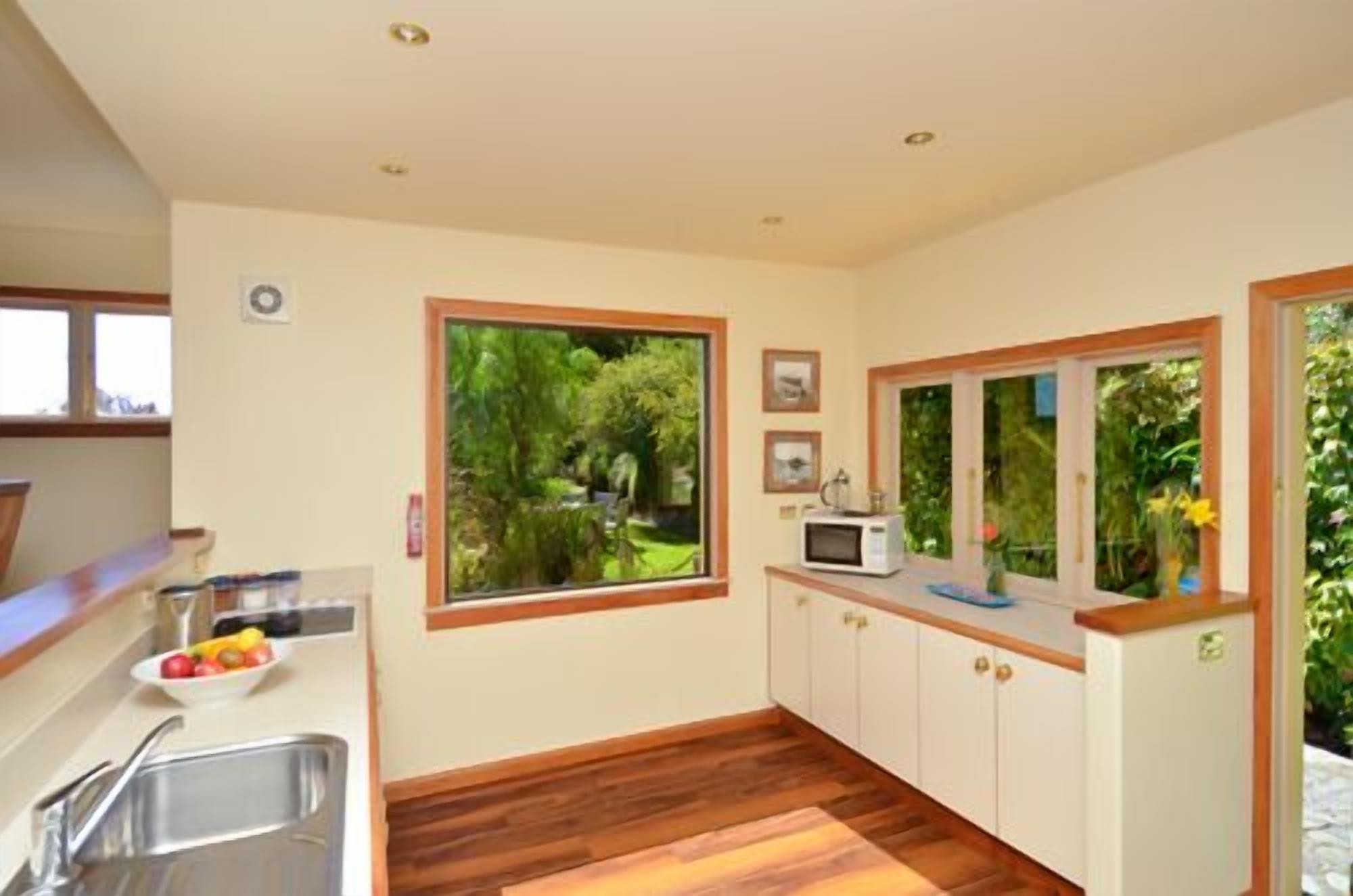 A kitchen with a large window, wooden cabinets, a microwave, and a sink.