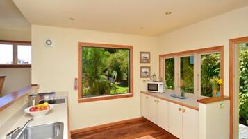 A kitchen with a large window, wooden cabinets, a microwave, and a sink.