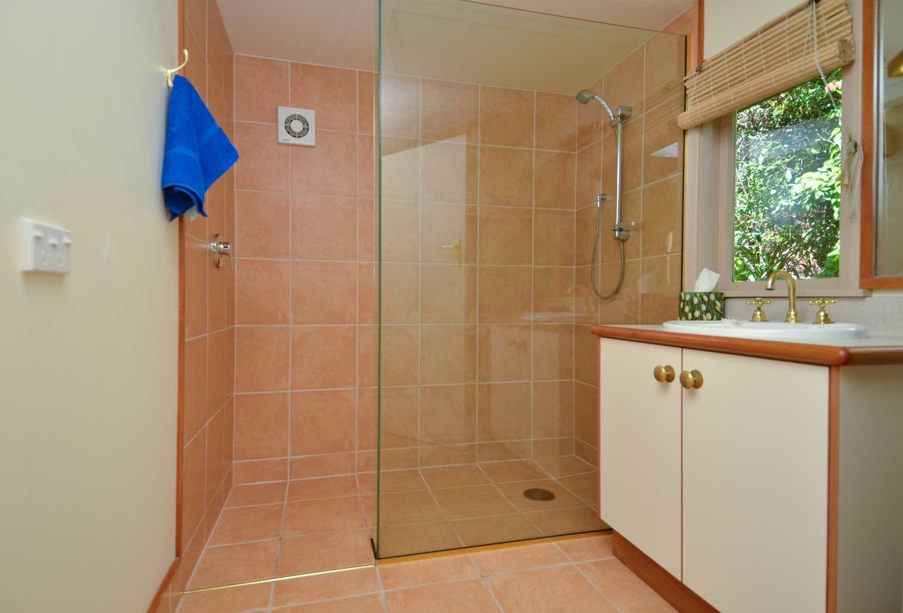 Une salle de bain avec une douche à parois de verre, un lavabo avec un miroir et une fenêtre donnant sur un espace verdoyant.