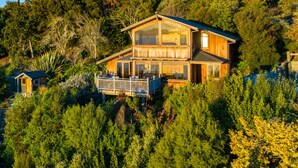 A two-story wooden cabin with large windows, a balcony, and surrounded by dense forest. - The Wheelhouse Inn (Nelson)