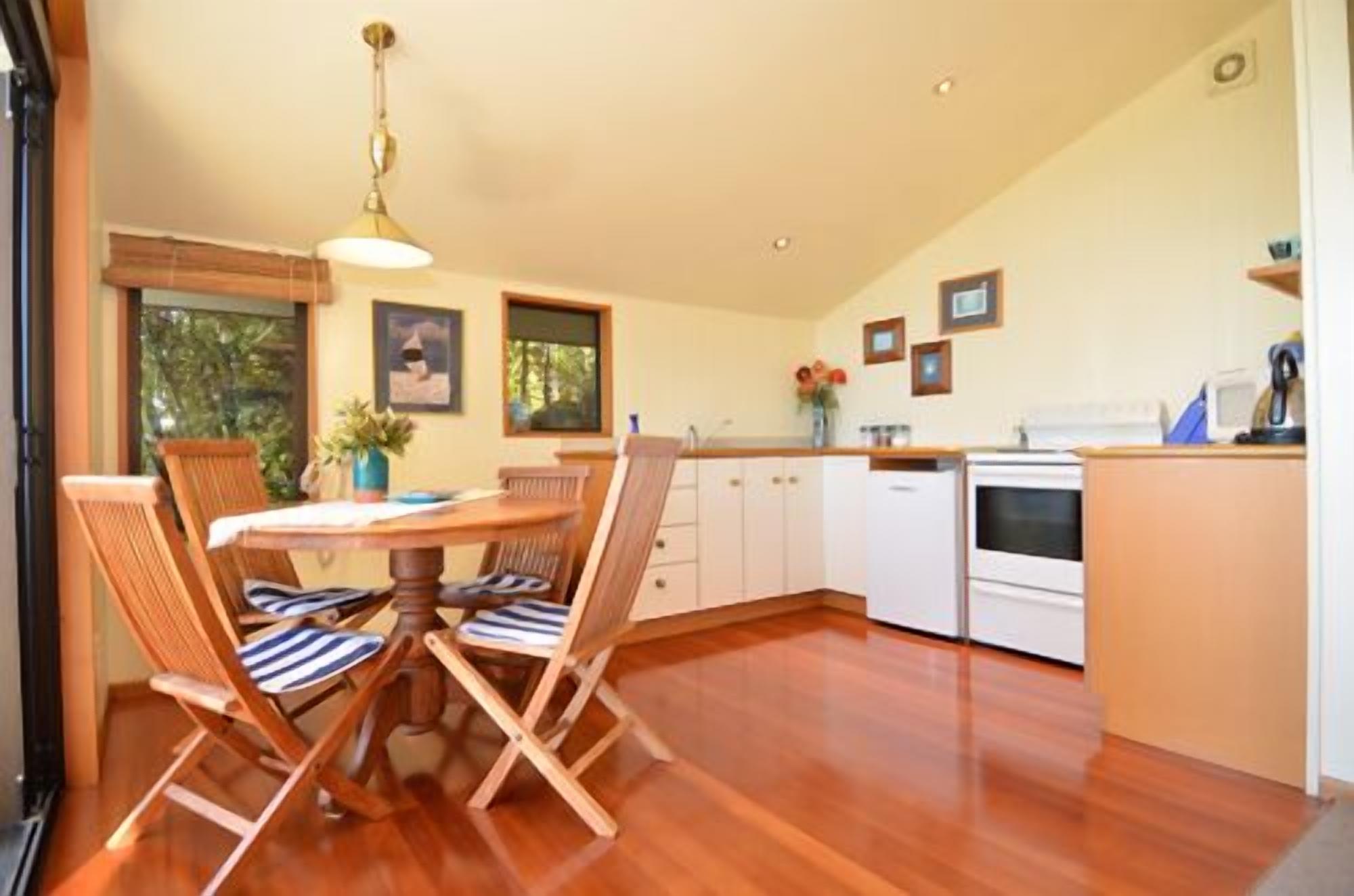 A spacious kitchen with wooden flooring, a dining area with a round table and striped chairs, and a view of the outdoors through large windows.