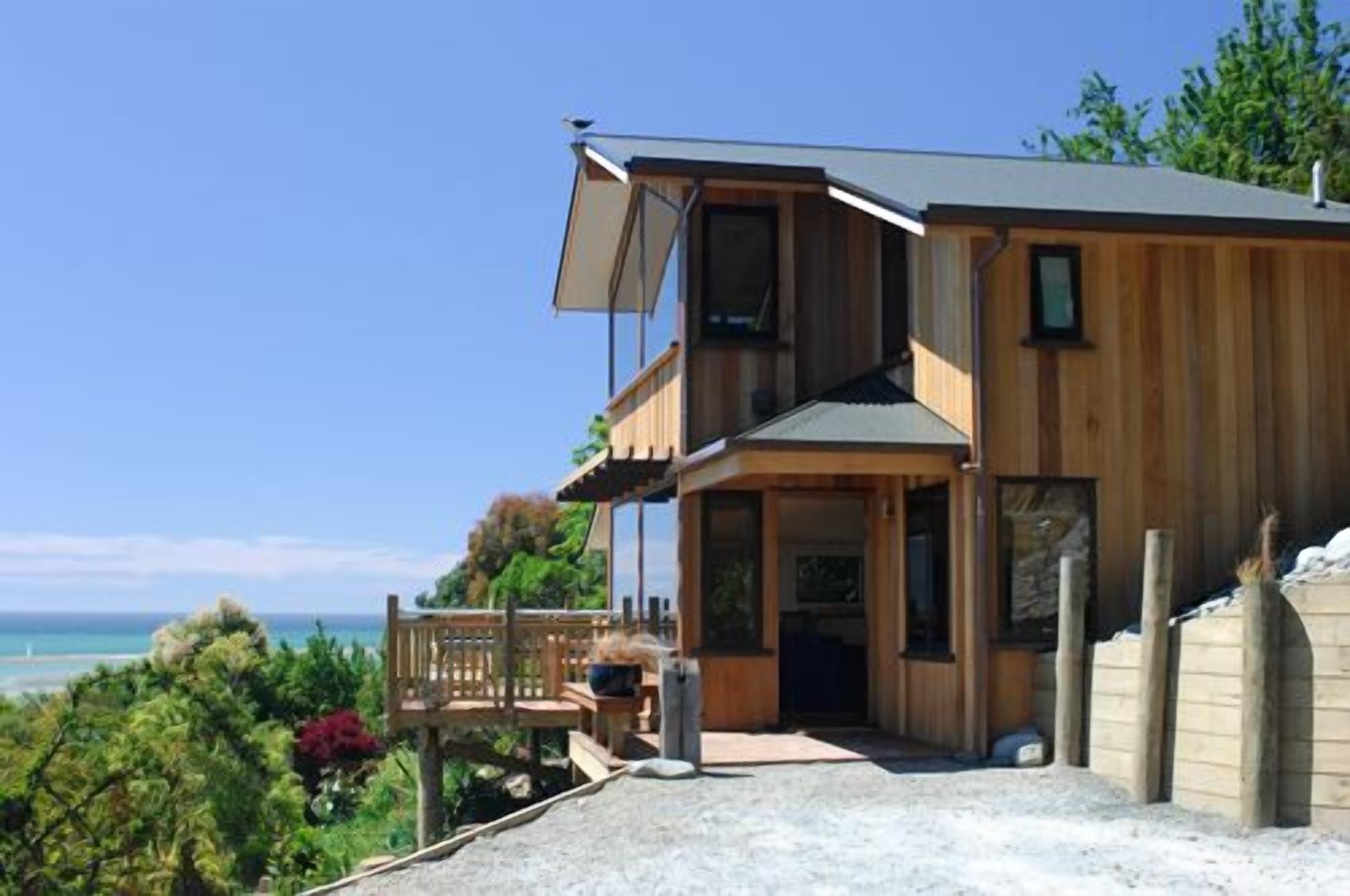 A two-story wooden house with a balcony, a covered porch, and a view of the ocean.