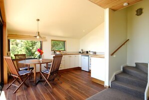 Una cocina amplia con suelo de madera, una zona de comedor con una mesa y sillas, y una escalera que sube a otro nivel.