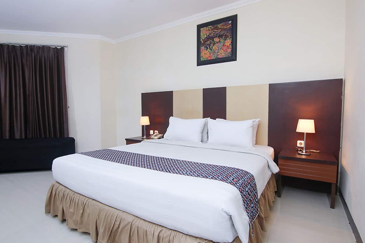 A hotel room with a large bed, two bedside tables with lamps, a dark headboard, and a painting on the wall.