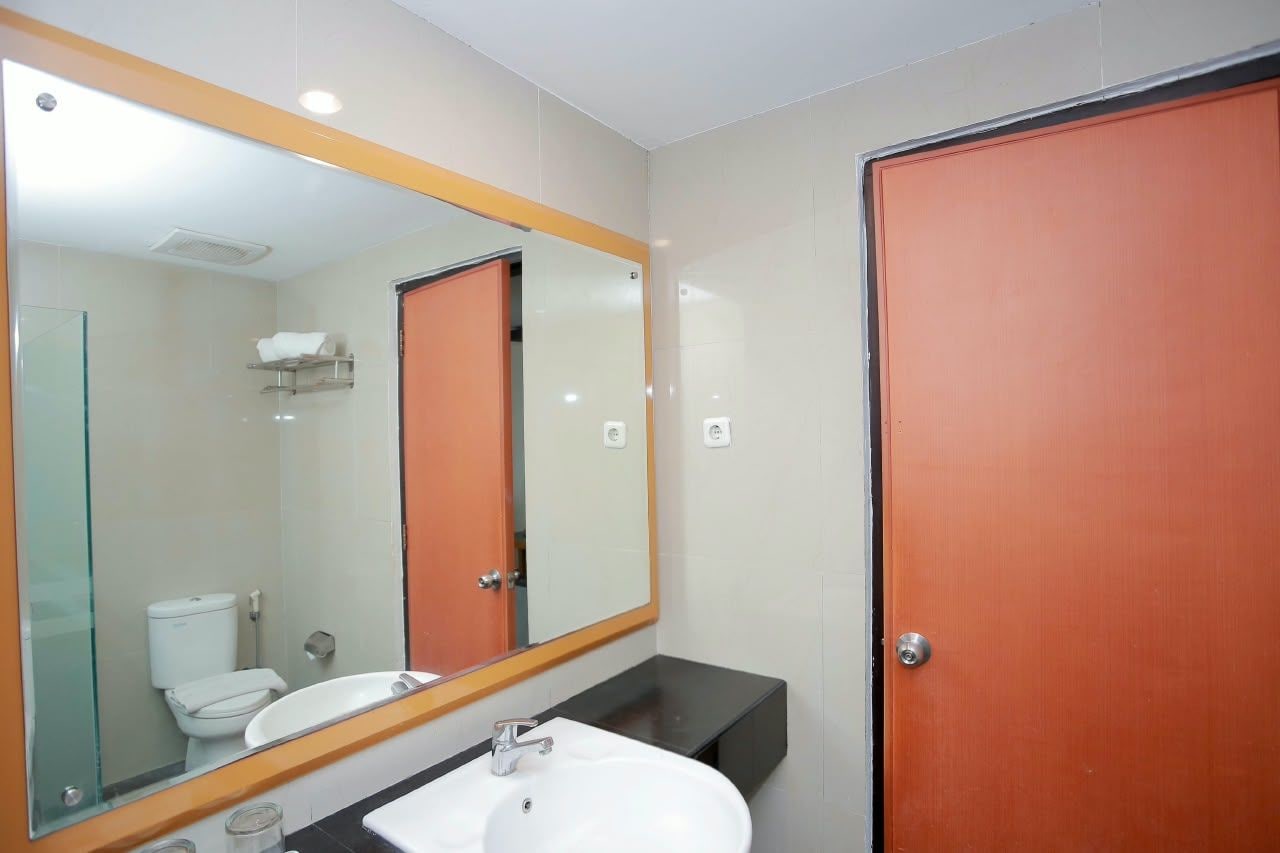 Un baño con lavamanos blanco, espejo y retrete.